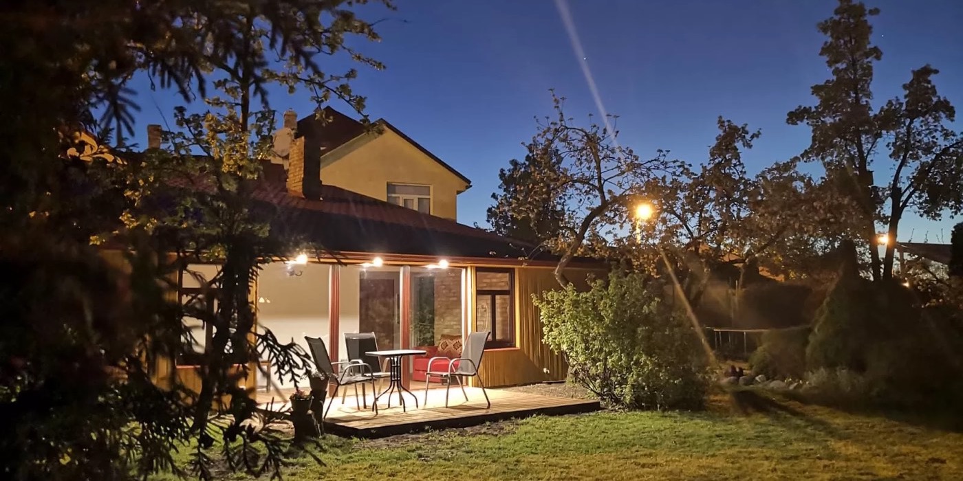 Viesu mājas AMRAI ēka vakara apgaismojumā ar zaļu pagalmu